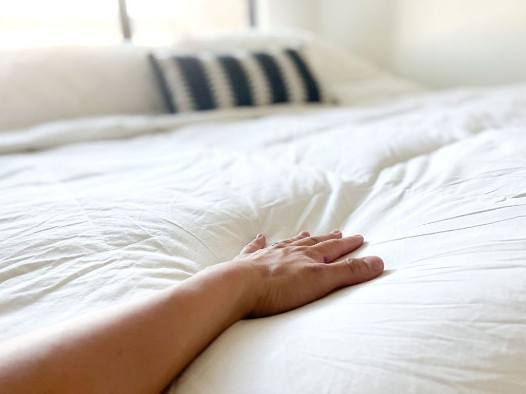 hand touching white down comforter on bed