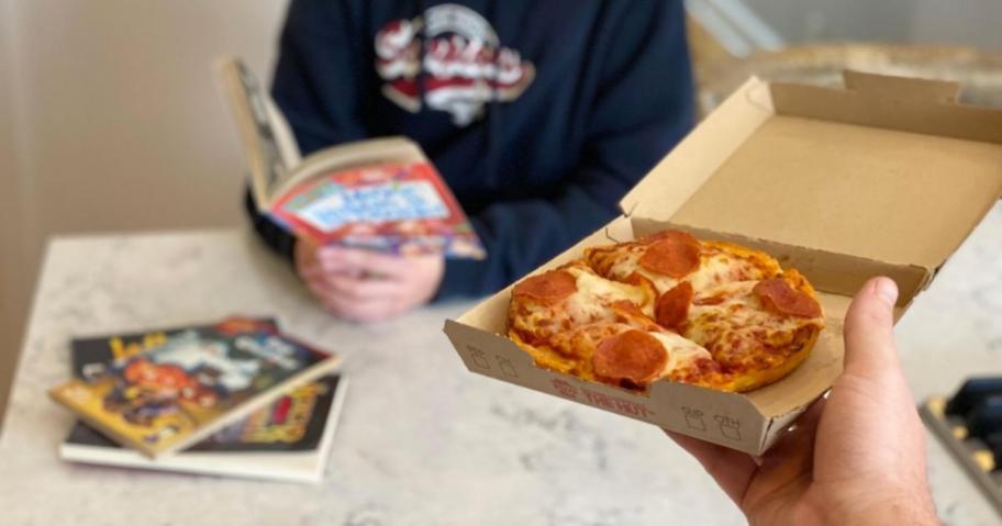 hand holding a personal pepperoni pizza in a box