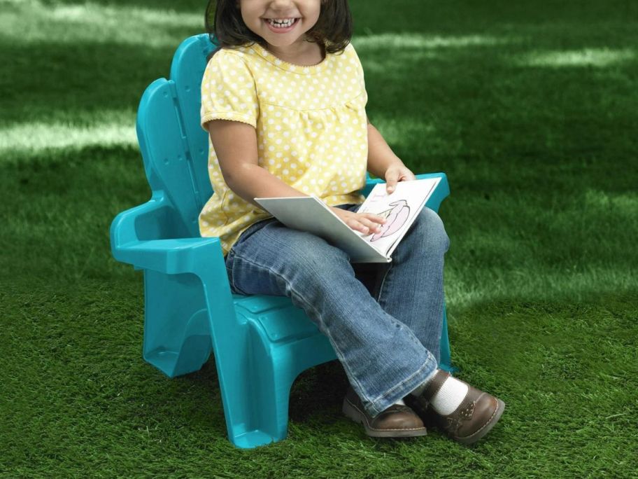 A child sitting in an Adirondack Chair on the lawn