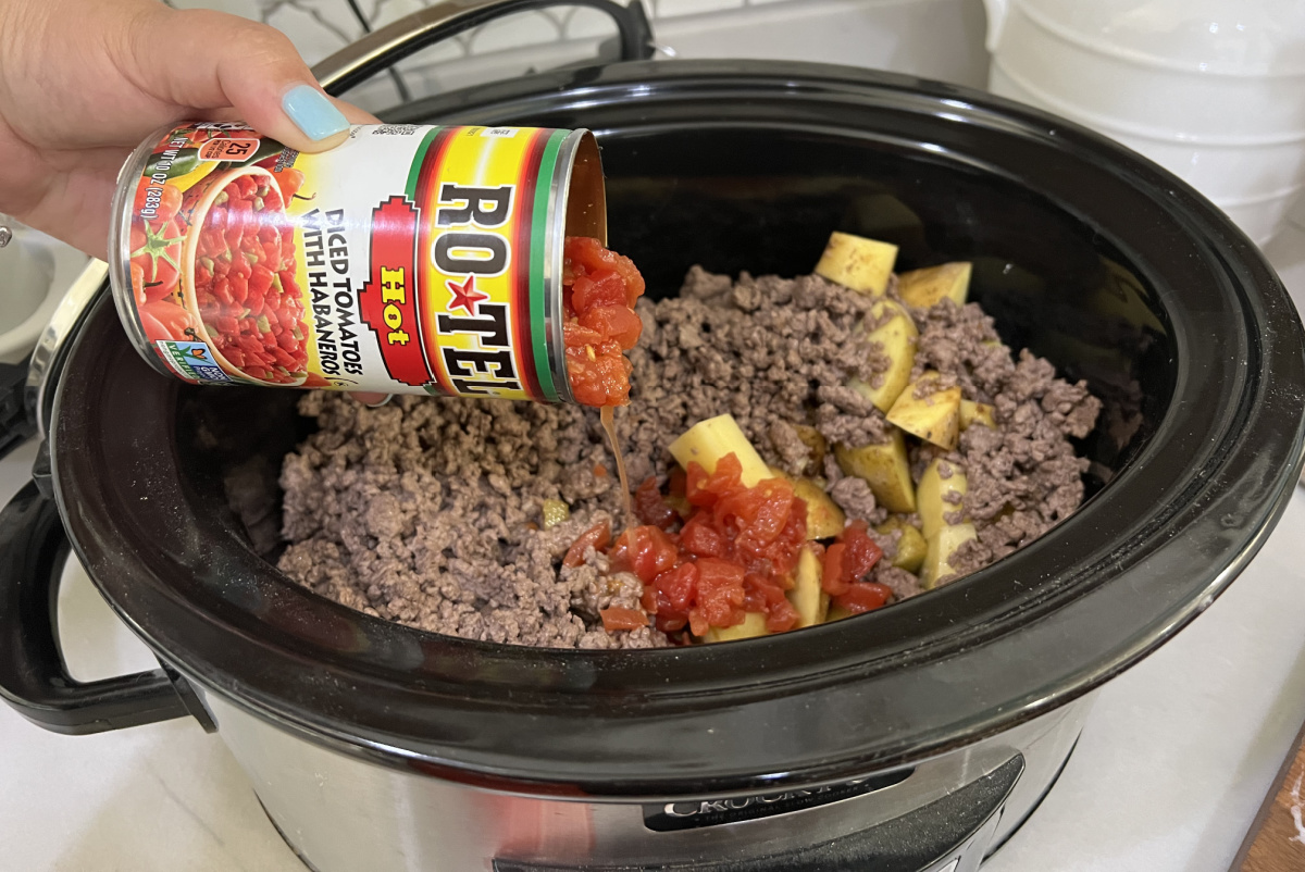Pouring a can of tomatoes into a cowboy casserole crock pot meal