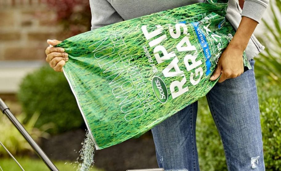 a person pouring turf builder mix from a large bag into a spreader