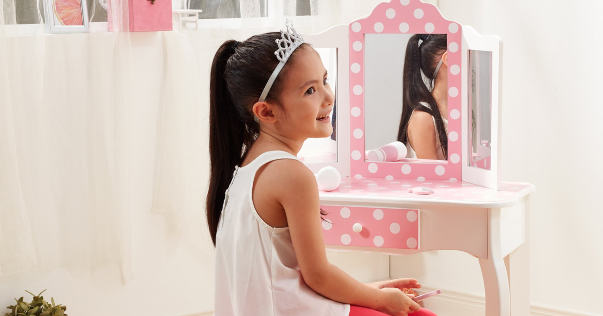 young girl wearing a princess crown sitting in front of a pink and white vanity