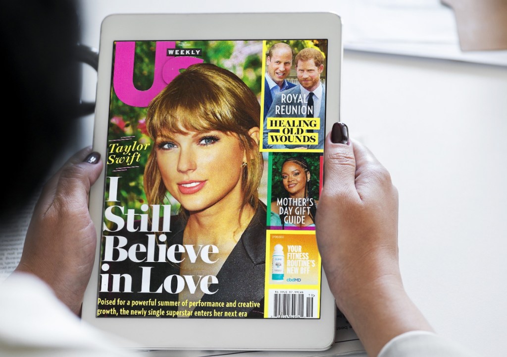 holding an ipad with us weekly magazine on screen