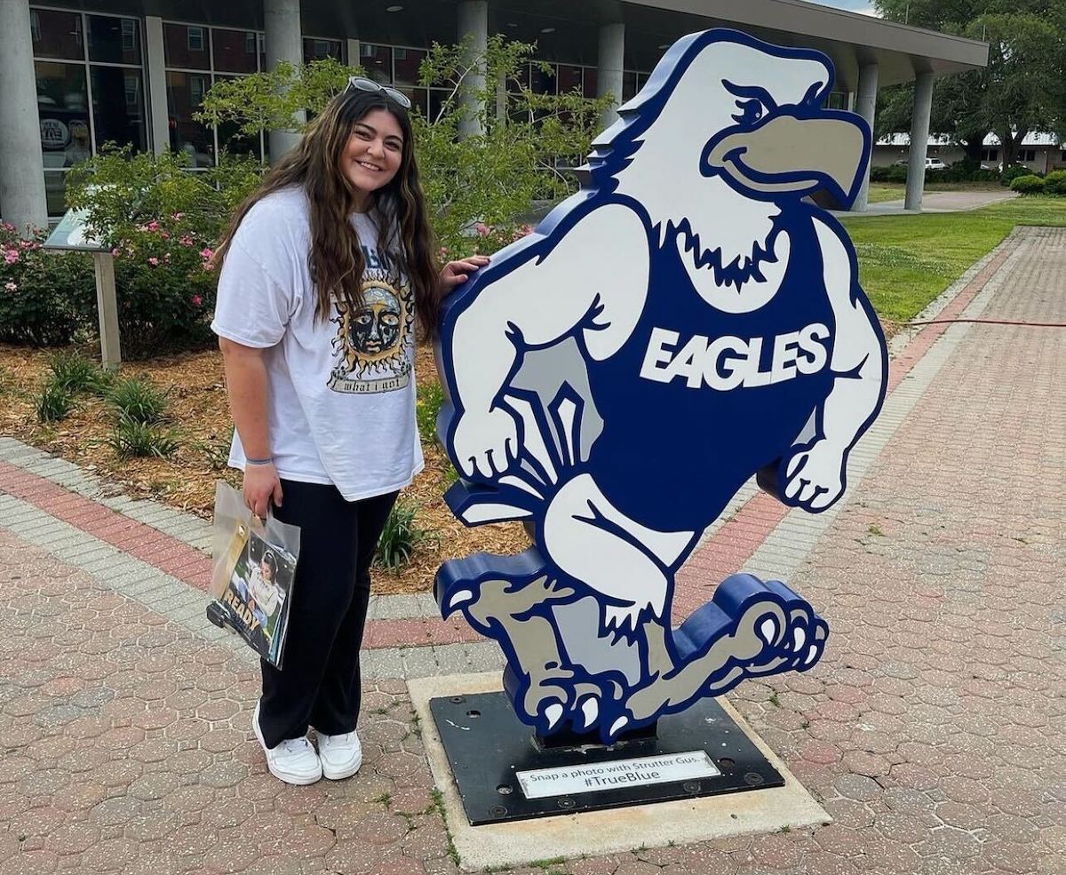 girl standing next to college mascot holding bag