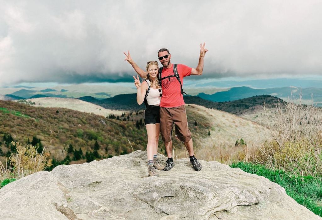 woman and man standing on cliff wearing hiking gear in mountains