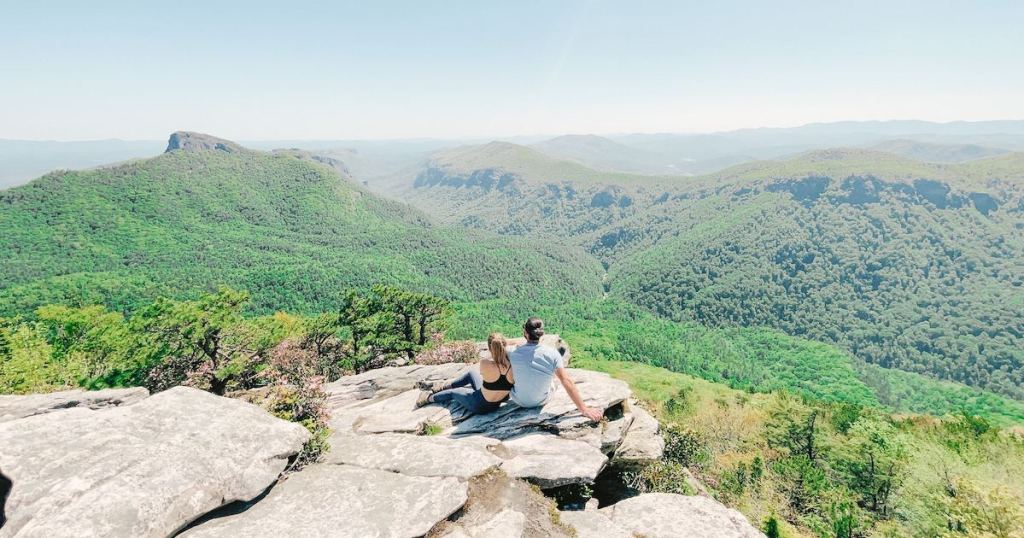 two people sitting on cliff rock in mountains