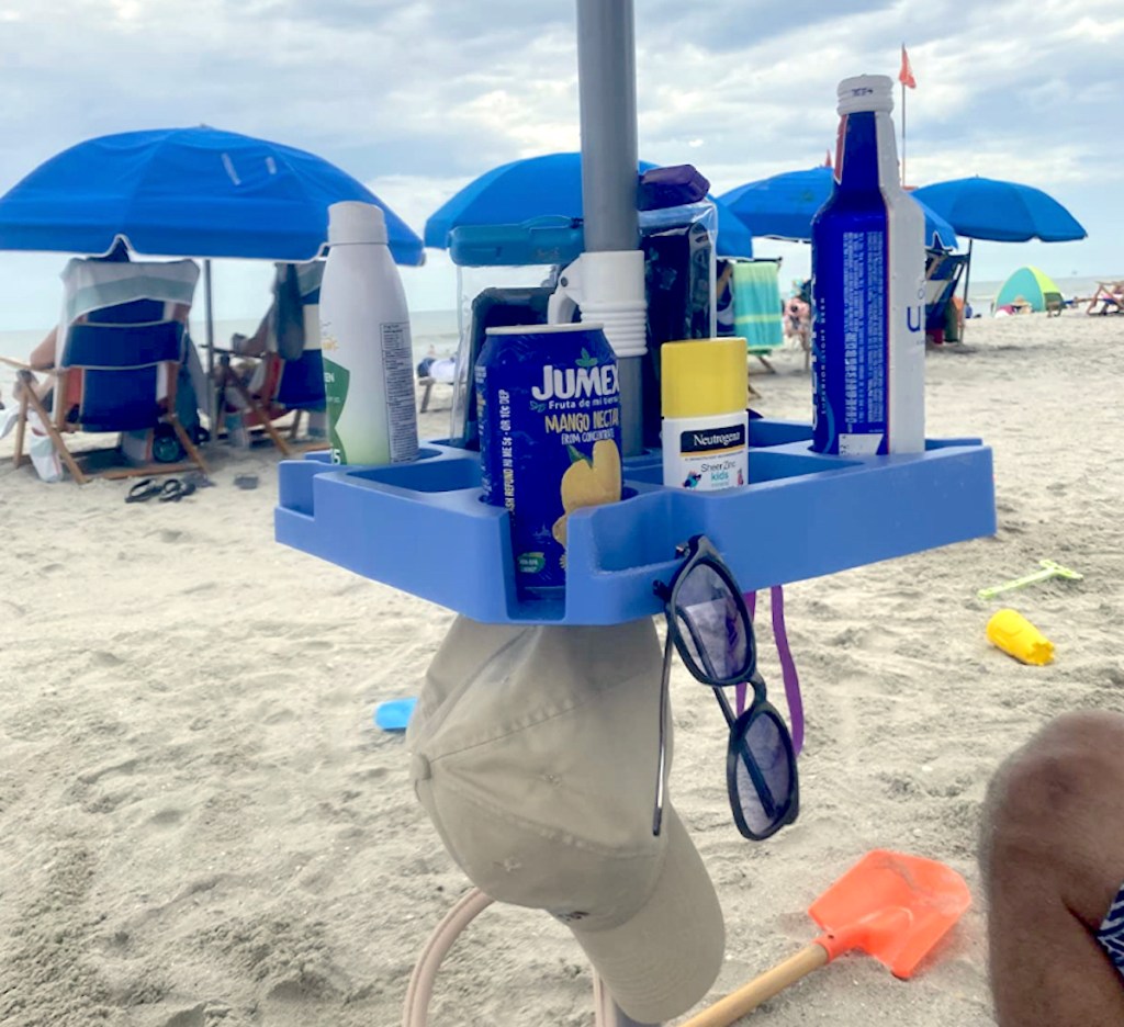 blue tray on beach umbrella with drinks sunscreen sunglasses and hat