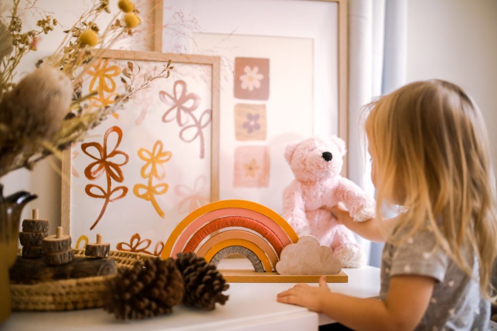 girl putting pink stuffed bear back on dresser next to rainbow stacking toy house cleaning tips