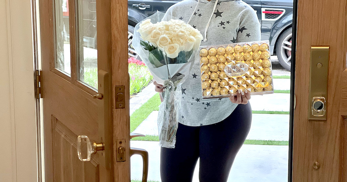 woman holding grocery door flowers and chocolates in front of door with instacart delivery