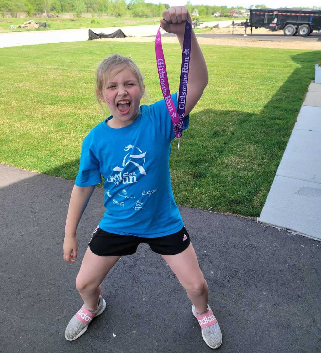 excited girl holding up medal from 5k run