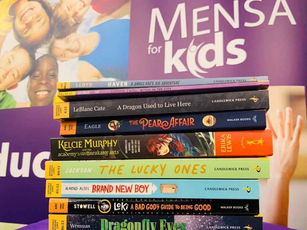 stack of children's chapter books in front of Mensa sign