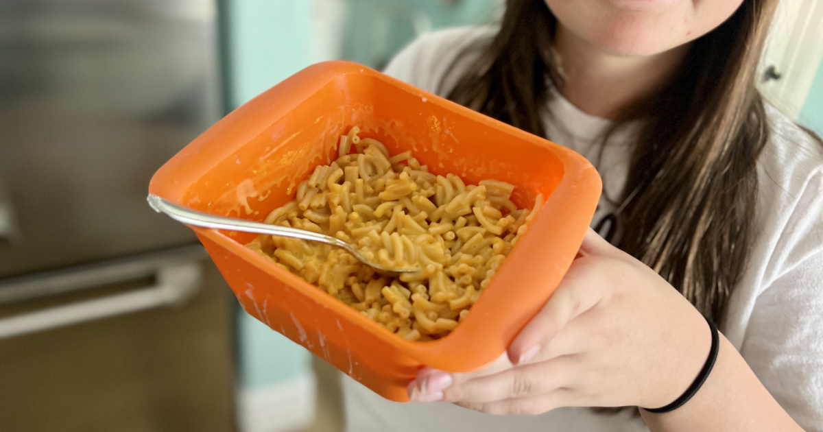 young girl holding a plastic container full of mac and cheese