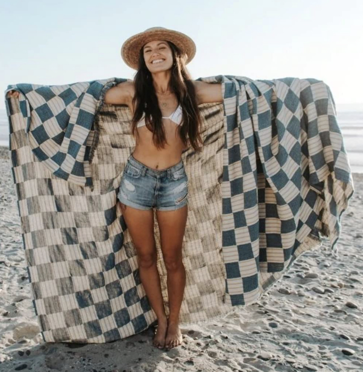woman holding checked beach towel blanket in sand