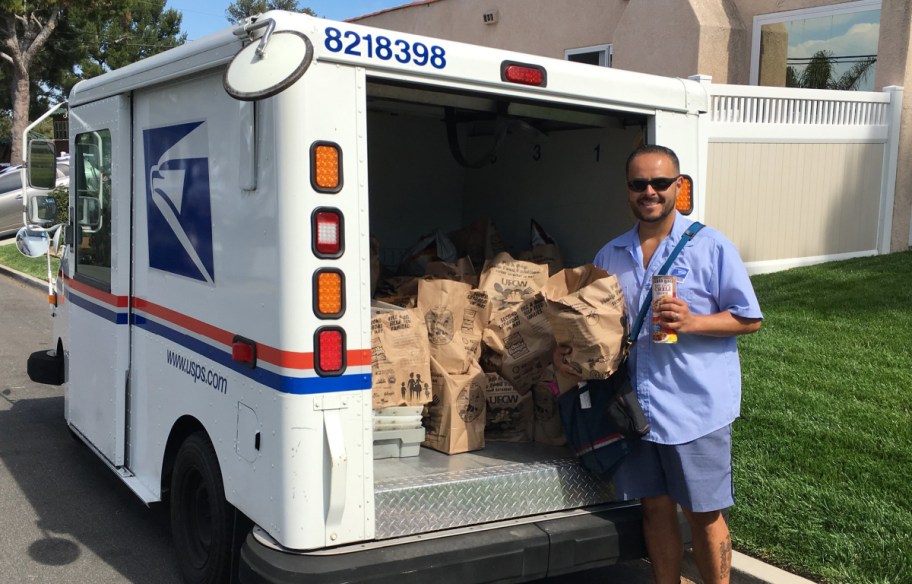 postal worker standing behind a mail carrying truck full of stamp out hunger food drive donations