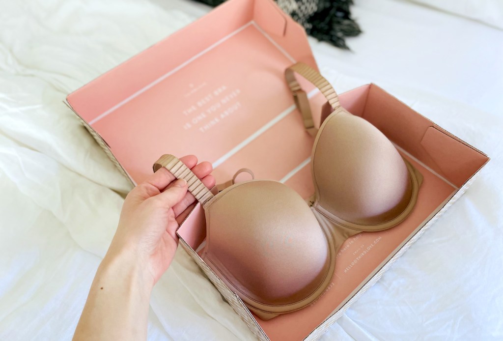 hand holding a strap from nude bra from thirdlove bras box on white sheet