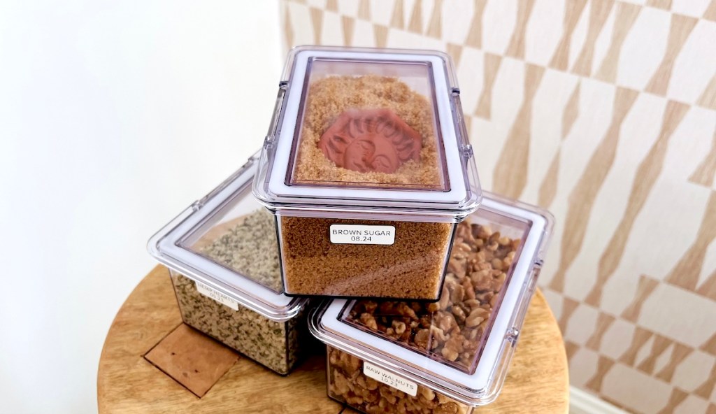 three clear food storage containers with dry food on wood side table the home edit products