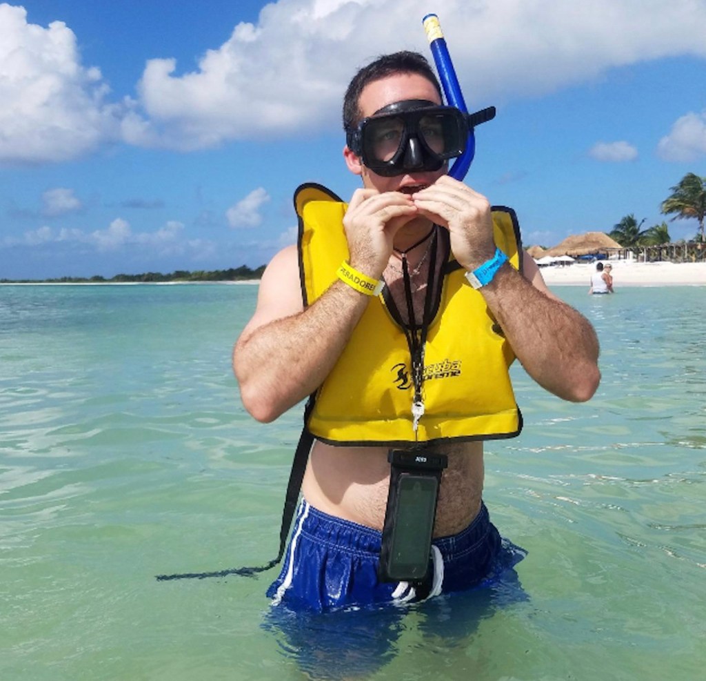 man in blue ocean with snorkel gear on face and waterproof phone case 