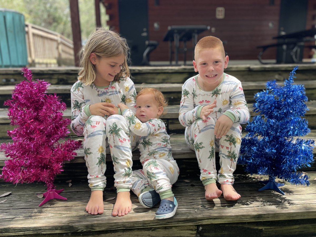 3 kids wearing matcing pajamas sitting next to colorful mini trees 