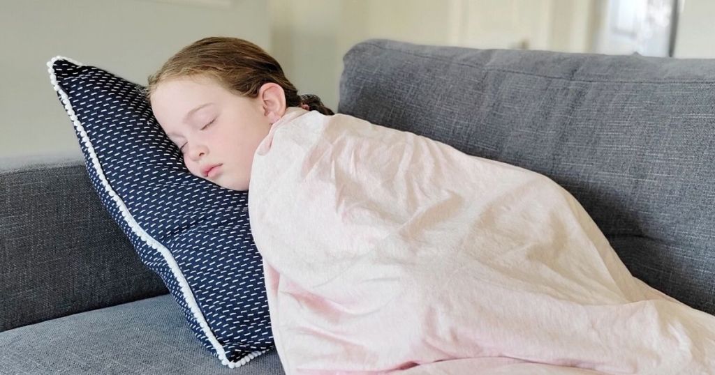 little girl wrapped in pink blanket sleepign on couch