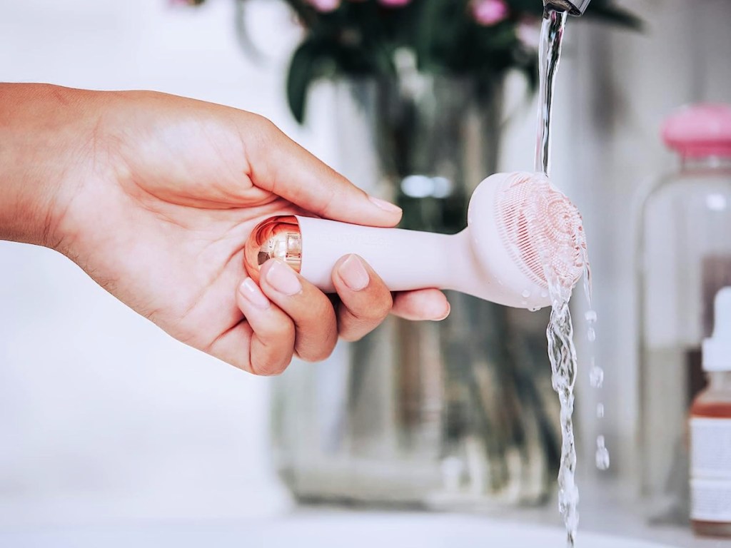 woman holding a Finishing Touch Flawless Cleanse Silicone Face Scrubber under running water