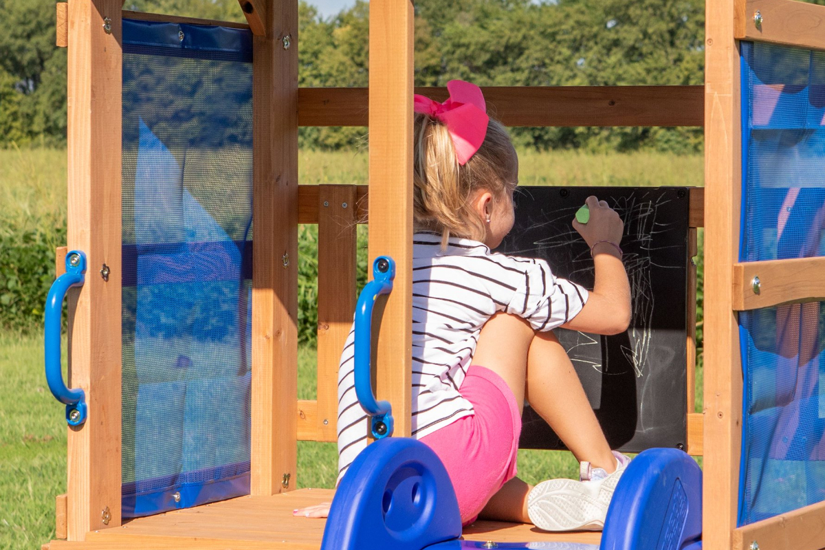 Girl drawing on chalkboard in clubhouse portion of a Backyard Discovery Swing Set
