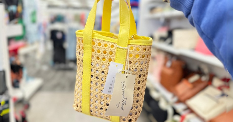 hand holding a small handbag with caning and yellow straps and accents