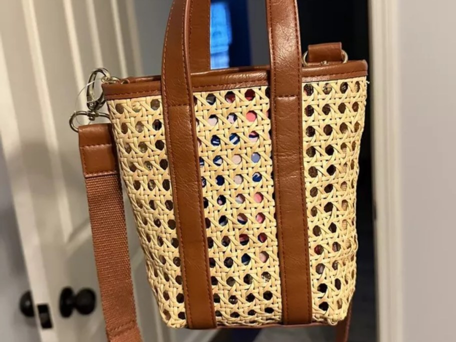 hand holding a small handbag with caning and brown straps and accents
