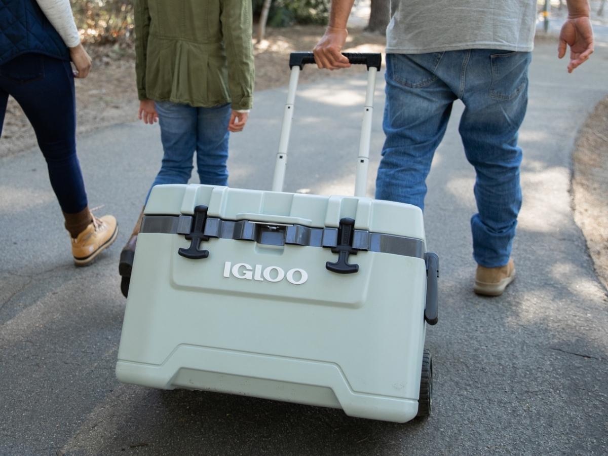 three people walking and pulling a large Igloo cooler with wheels and handle