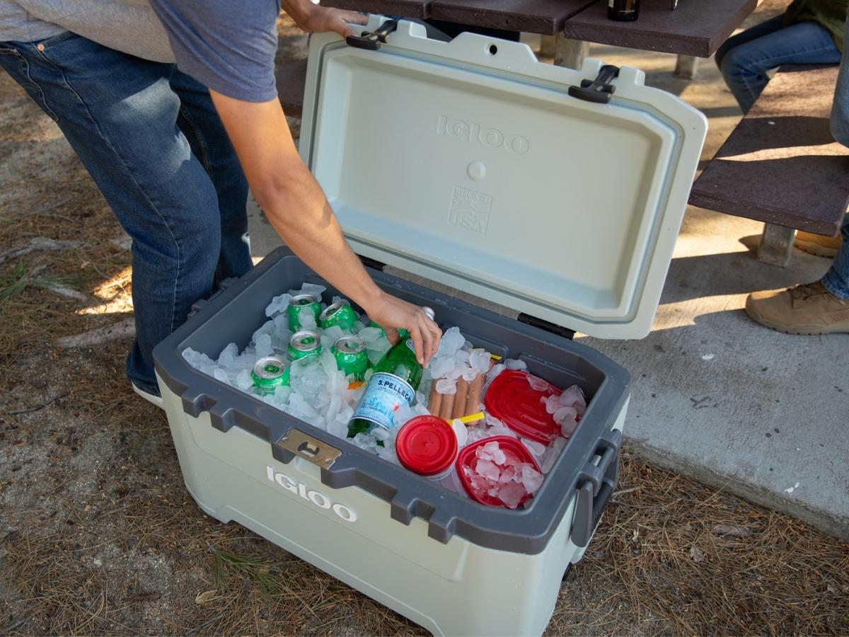 man reaching into an Igloo cooler filled with drinks, ice, and hotdogs