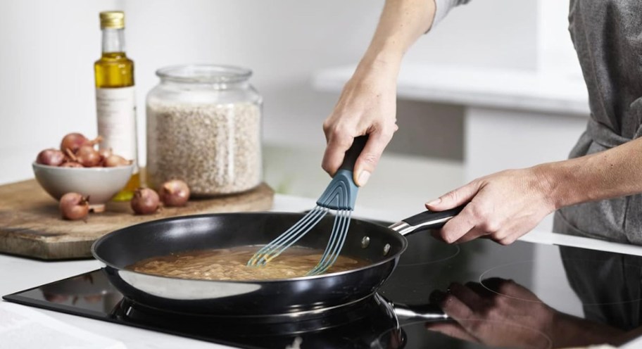Man cooking in the kitchen skillet on the stove using a flat whisk