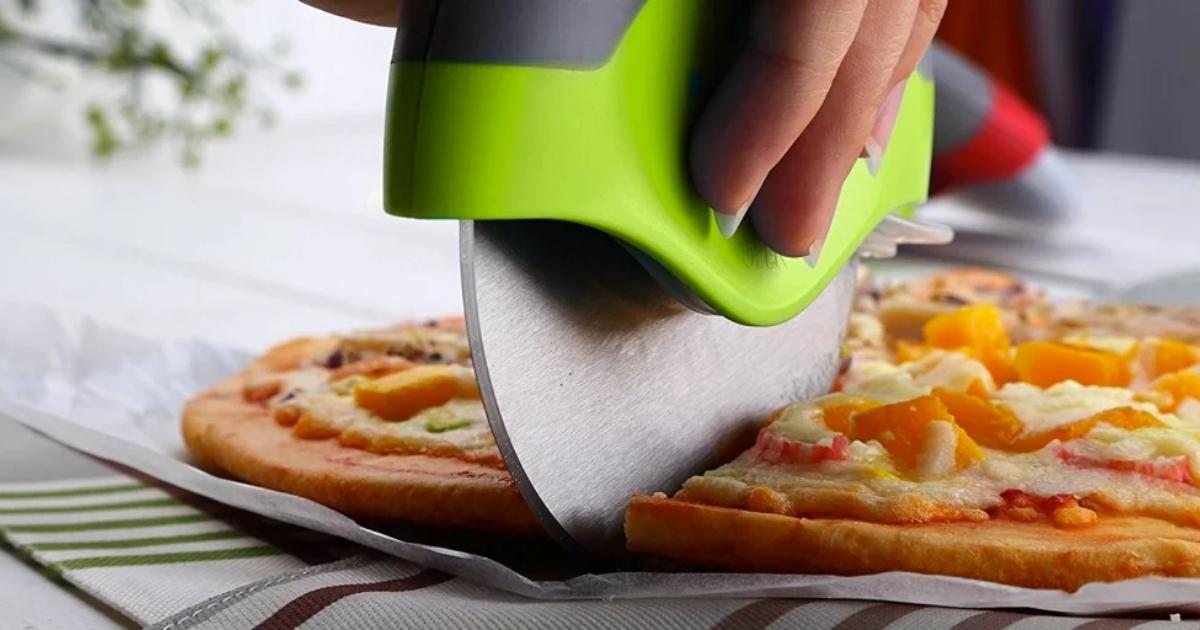 kitchy pizza cutter in green cutting through pizza