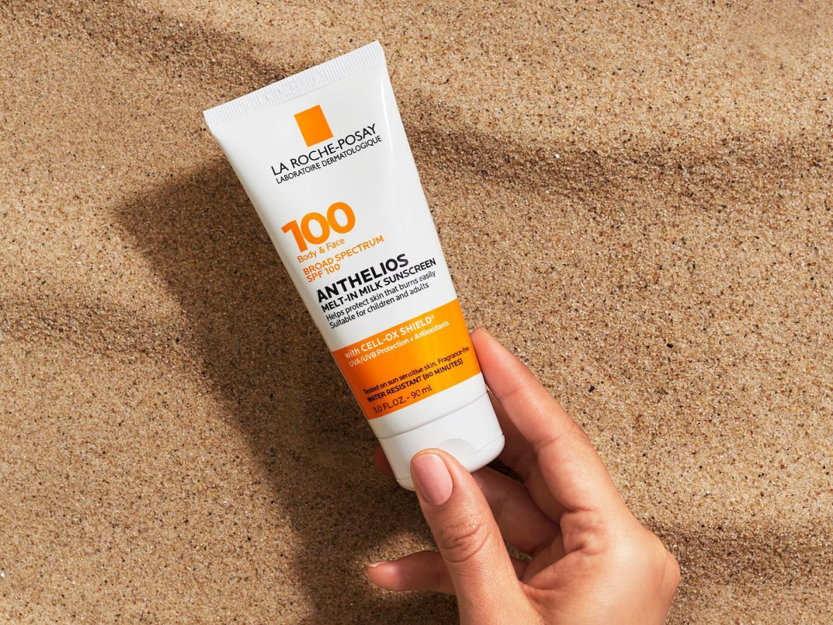 hand holding la roche-posay sunscreen over sand