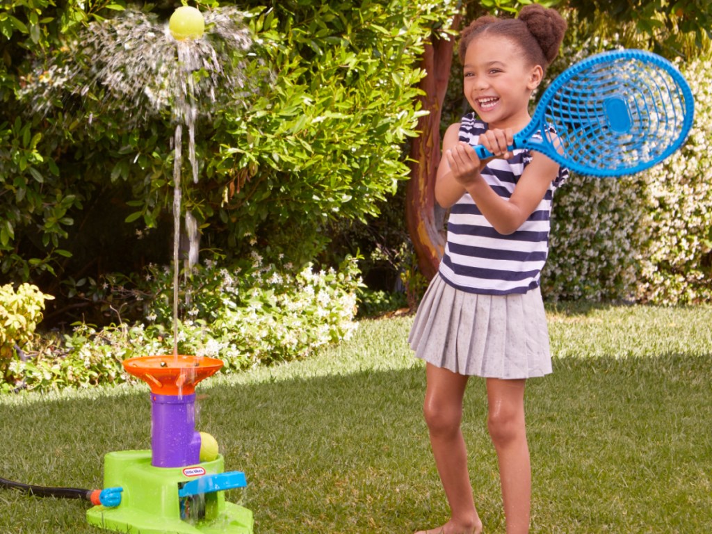 girl holding tennis racket and tennis water toy launching ball in yard