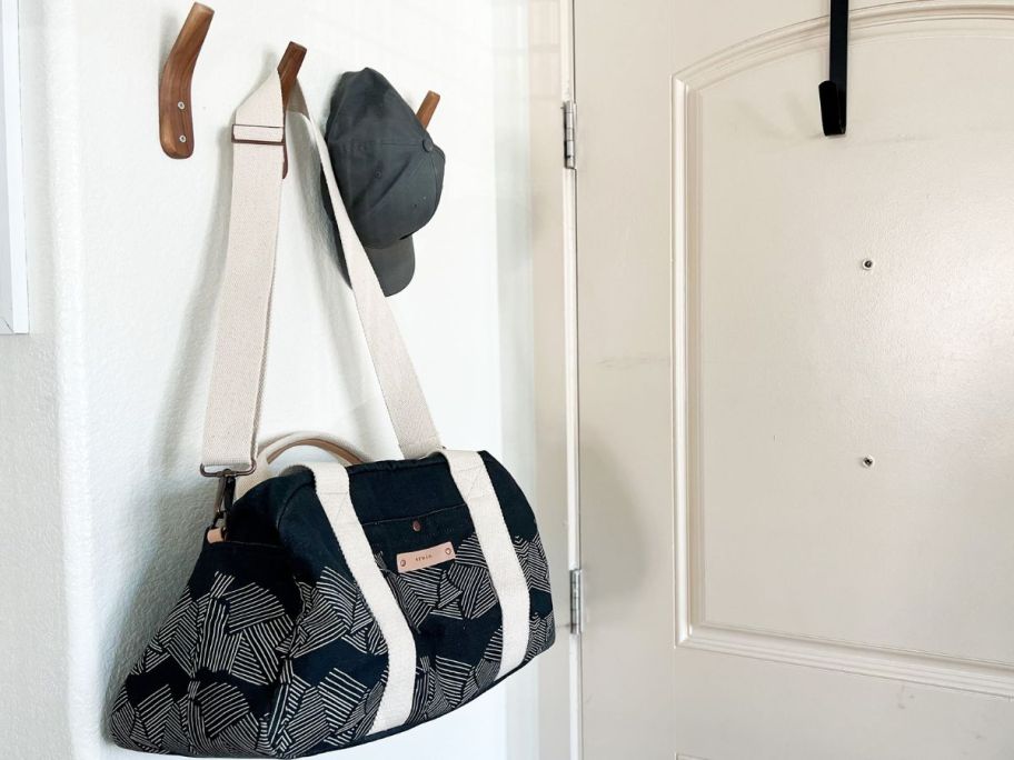 A wall rack with a baseball cap and a Minted weekender bag hanging on it