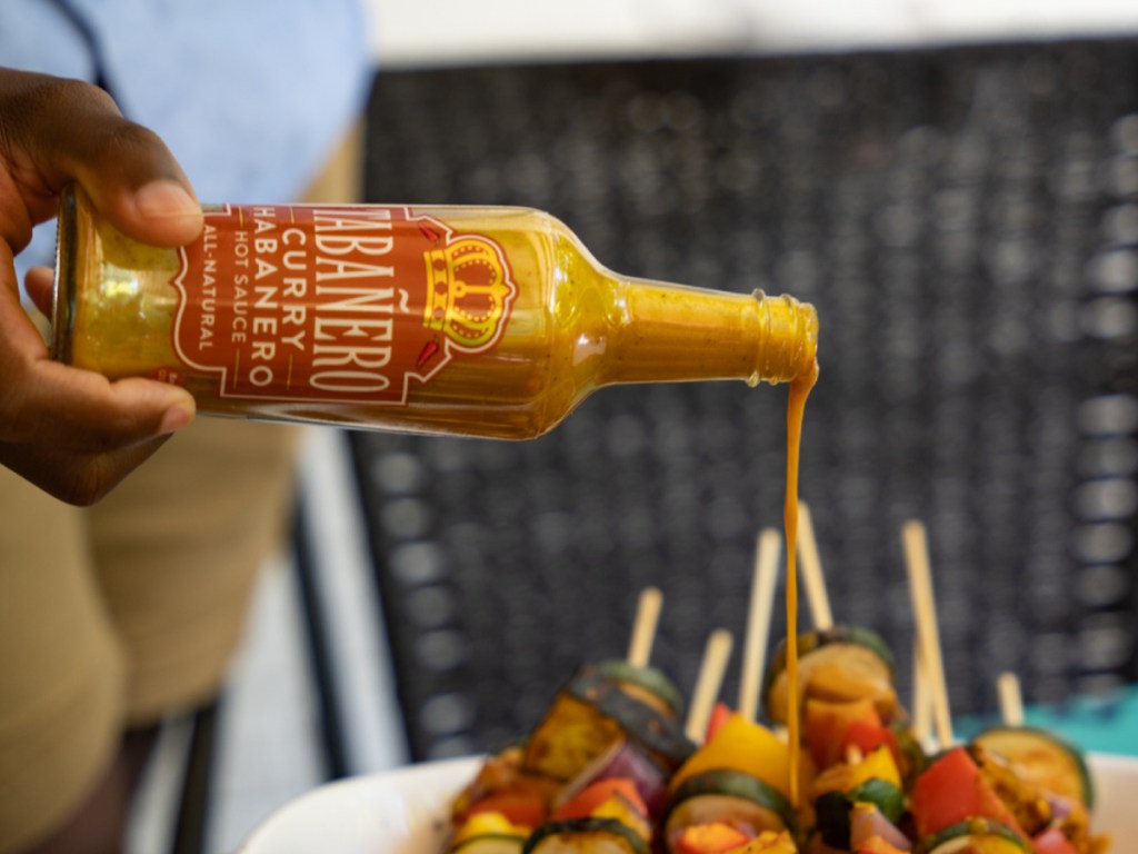 hand pouring curry habanero hot sauce on kebobs