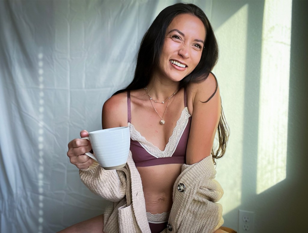 woman in bralette and sweater holding cup of coffee