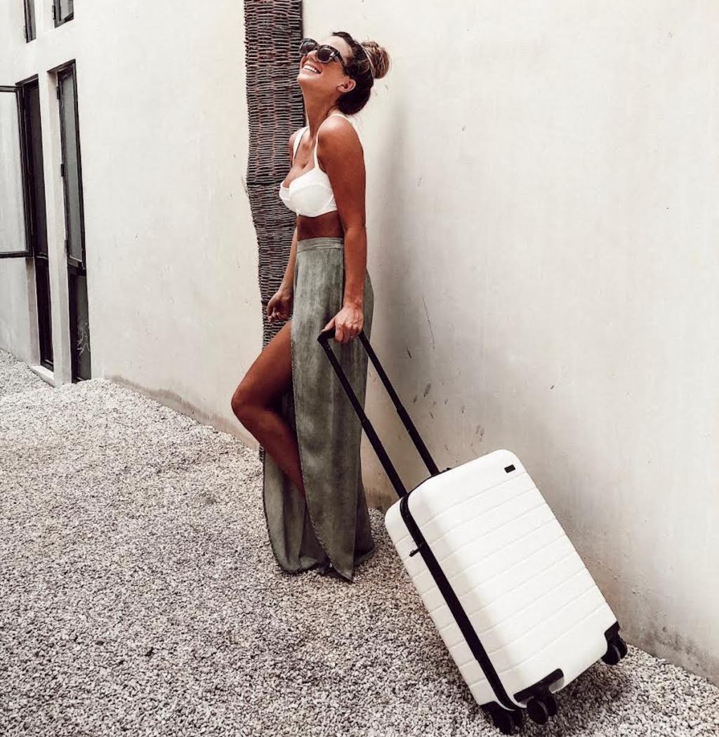 woman standing in front of wall with white away luggage suitcase