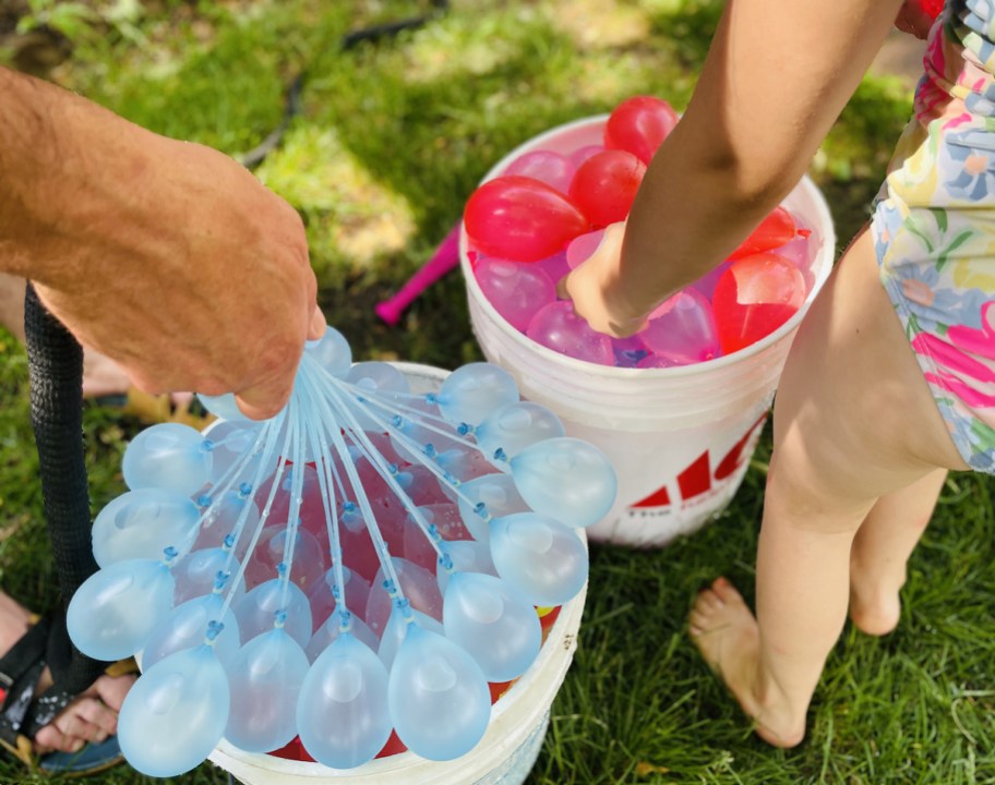 blue and pink water balloons in buckets outside in grass