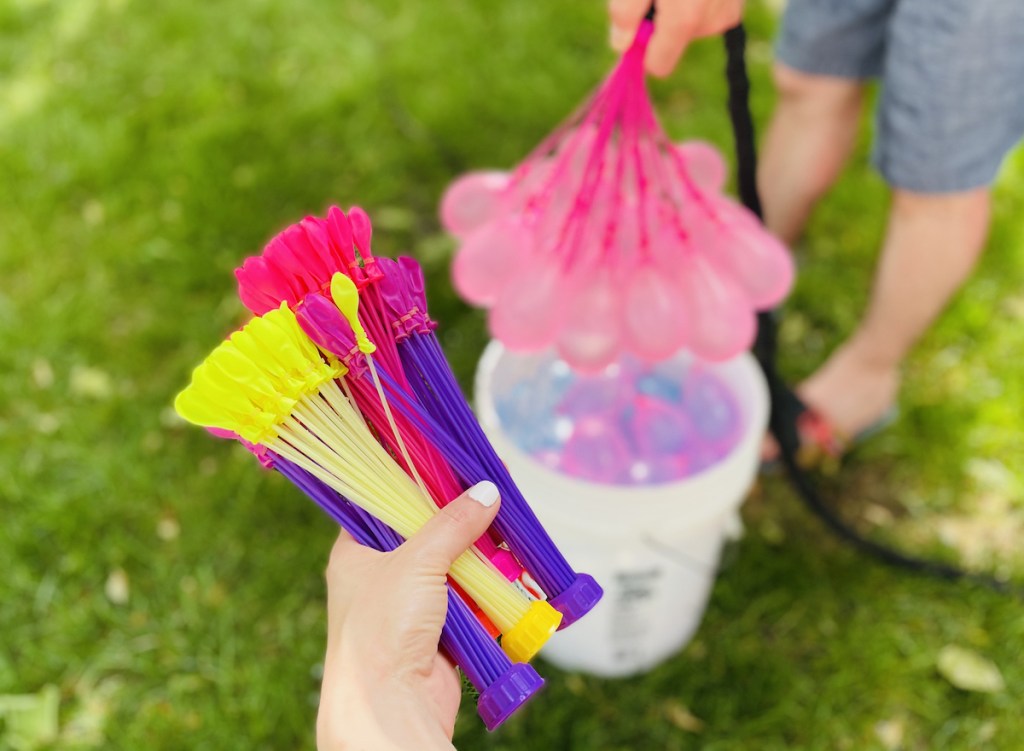 hand holding pack of water balloons with bucket full of them in background