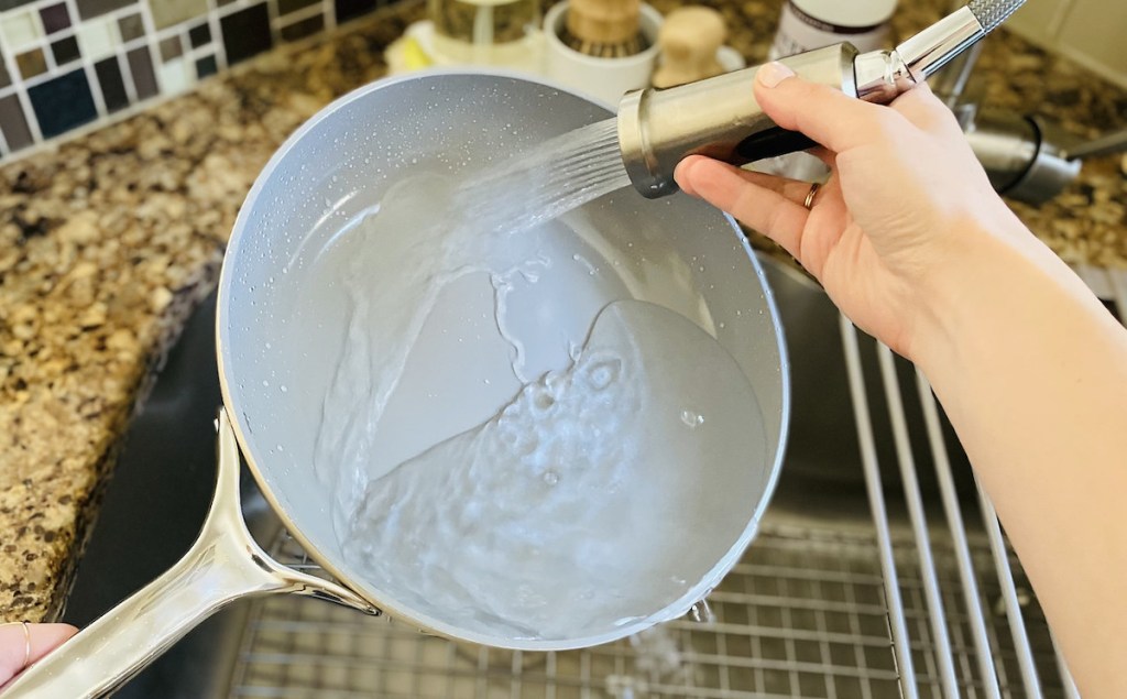 hand holding faucet sprayer on nonstick pan in sink