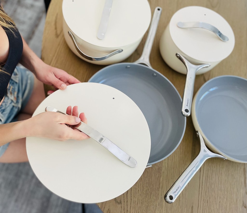 woman sitting at wood table taking lid of white pan