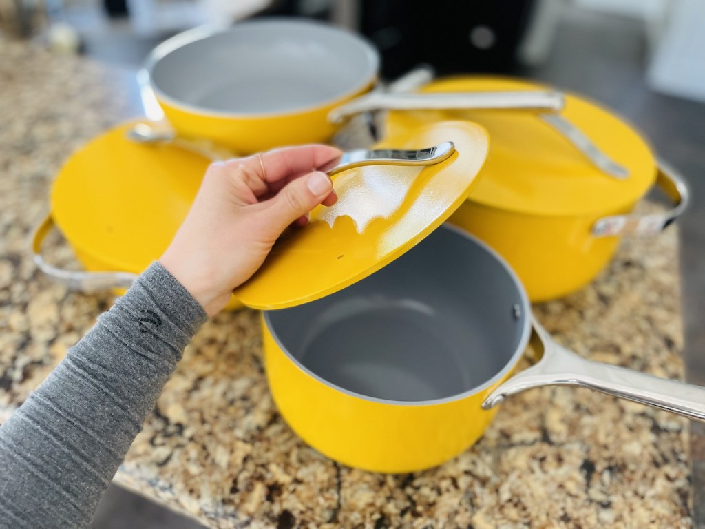 hand holding lid to yellow sauce pan 