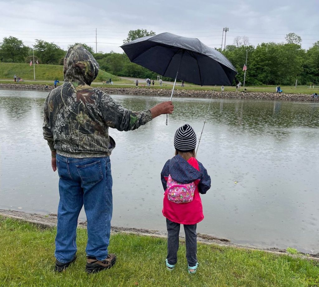 man holding umbrella over child's head standing next to river