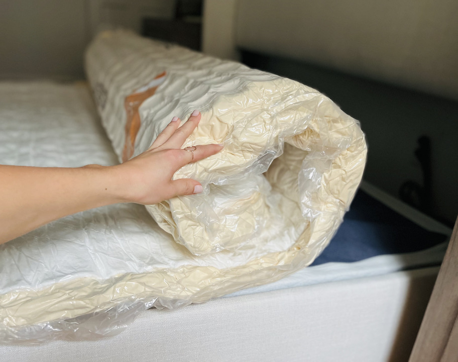 hand holding rolled up new mattress on bed frame