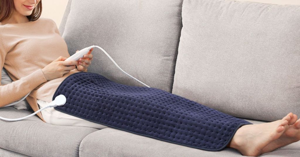 woman laying on couch using Evajoy Heating Pad on her legs
