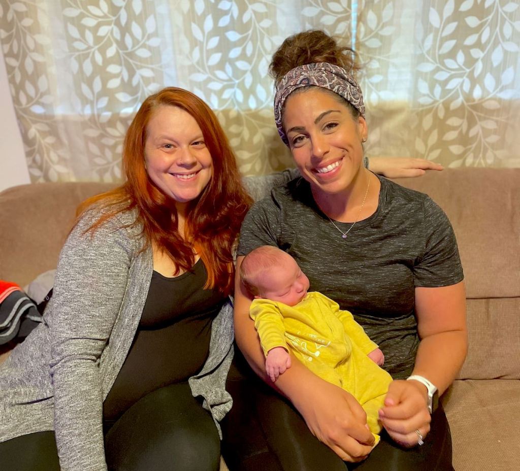 two women sitting on couch holding a newborn baby