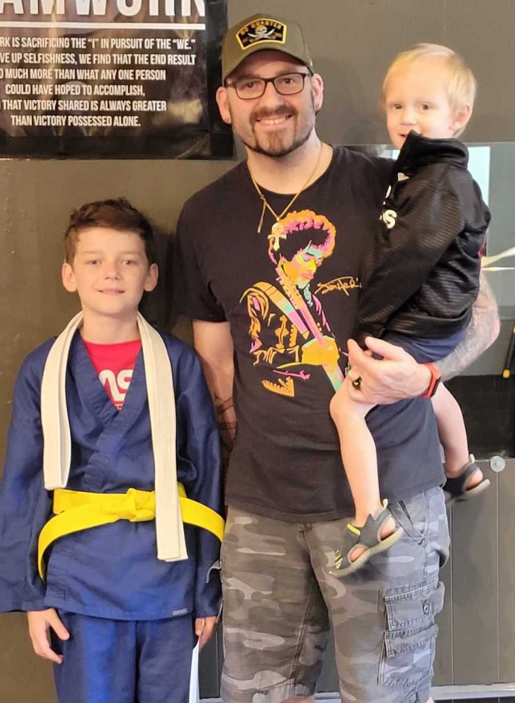 boy wearing Tae Kwon Do yellow belt standing with dad and baby brother