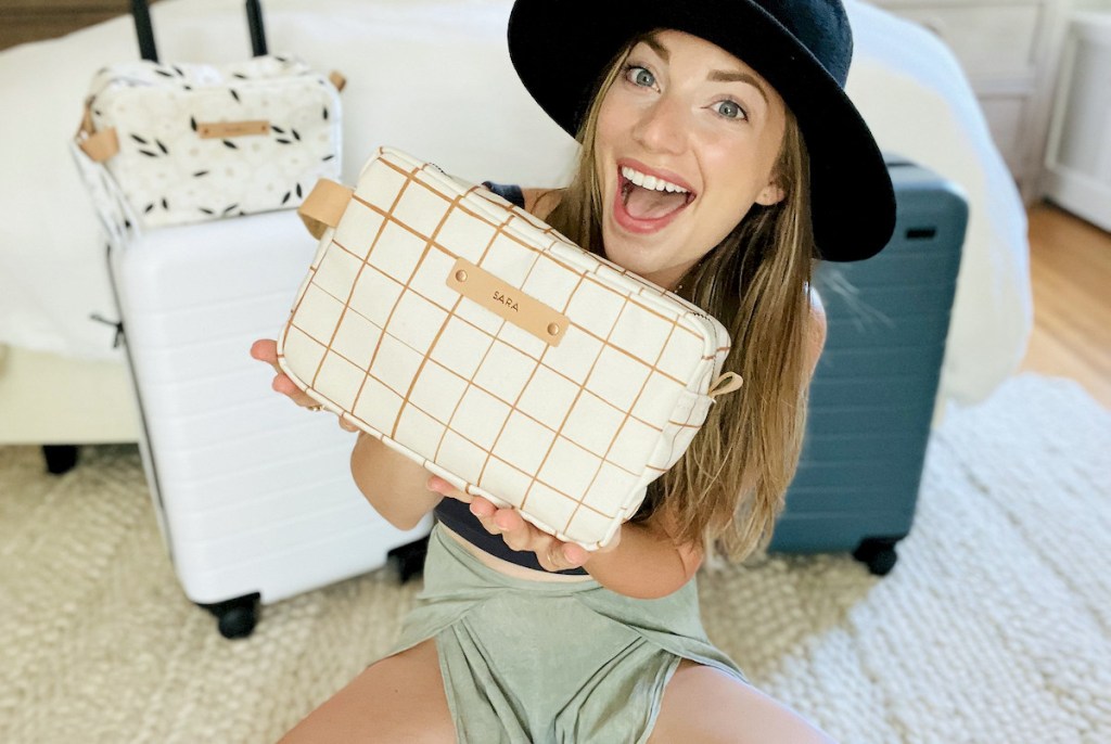 woman holding up a dopp kit toiletry bag with luggage