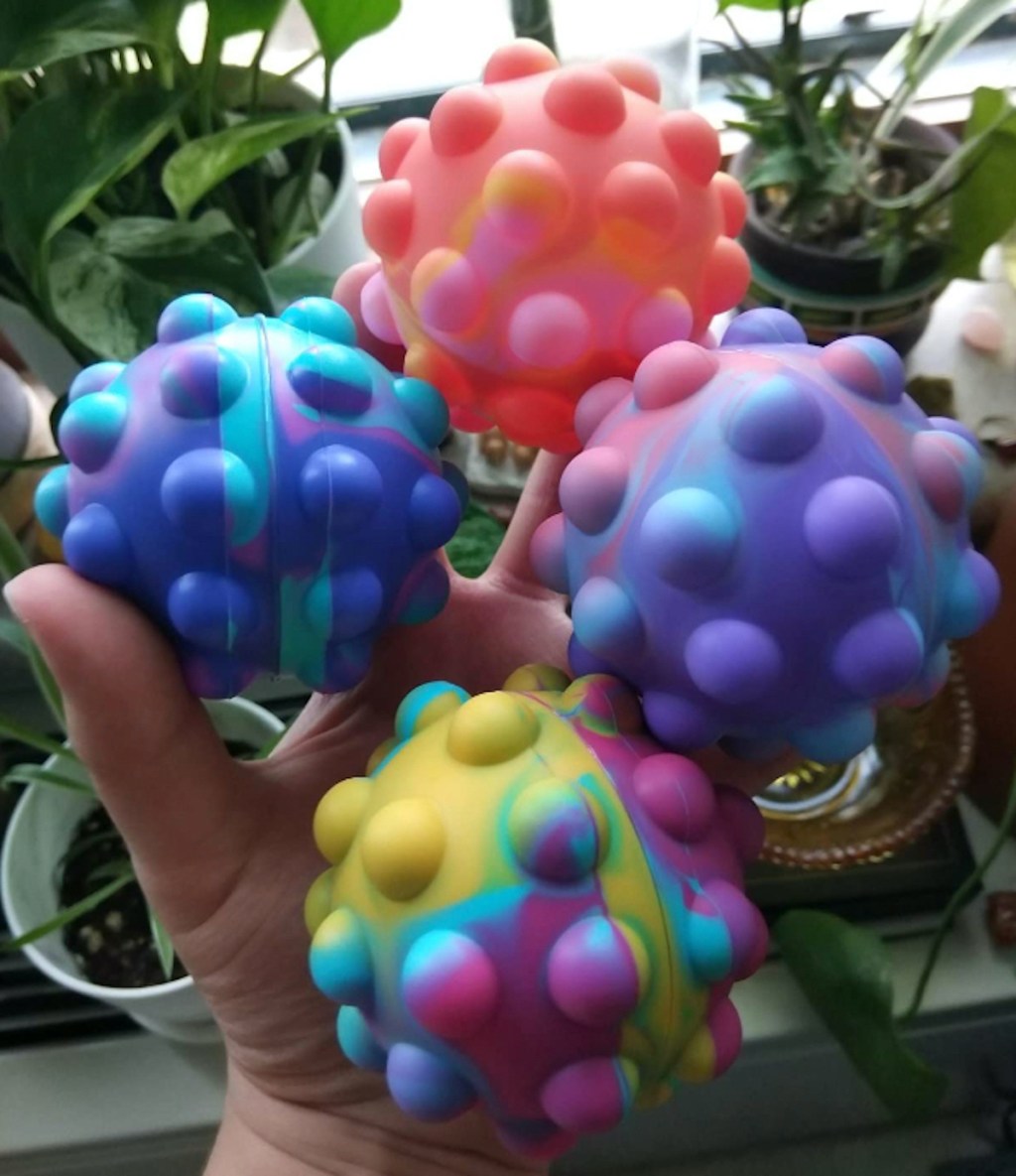 hand holding four pop ball fidget toys in front of plants