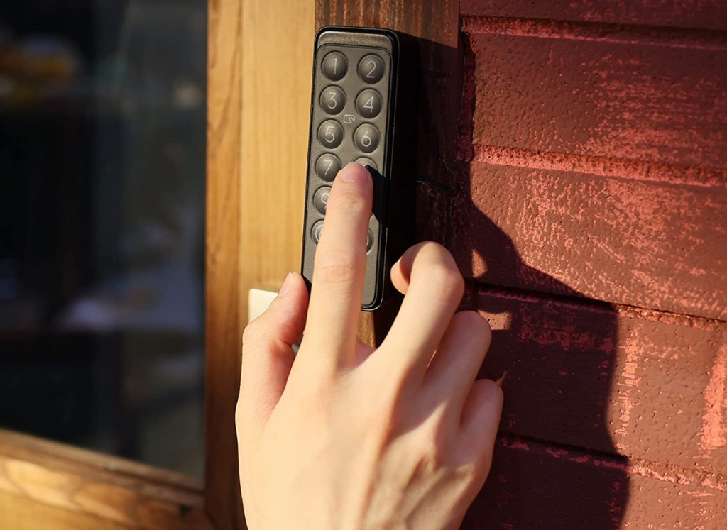 hand pressing buttons on a smart lock installed on a brick wall